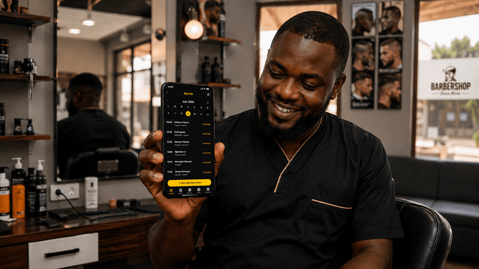 Coiffeur souriant tenant son téléphone, l'agenda des réservations du jour affiché à l'écran