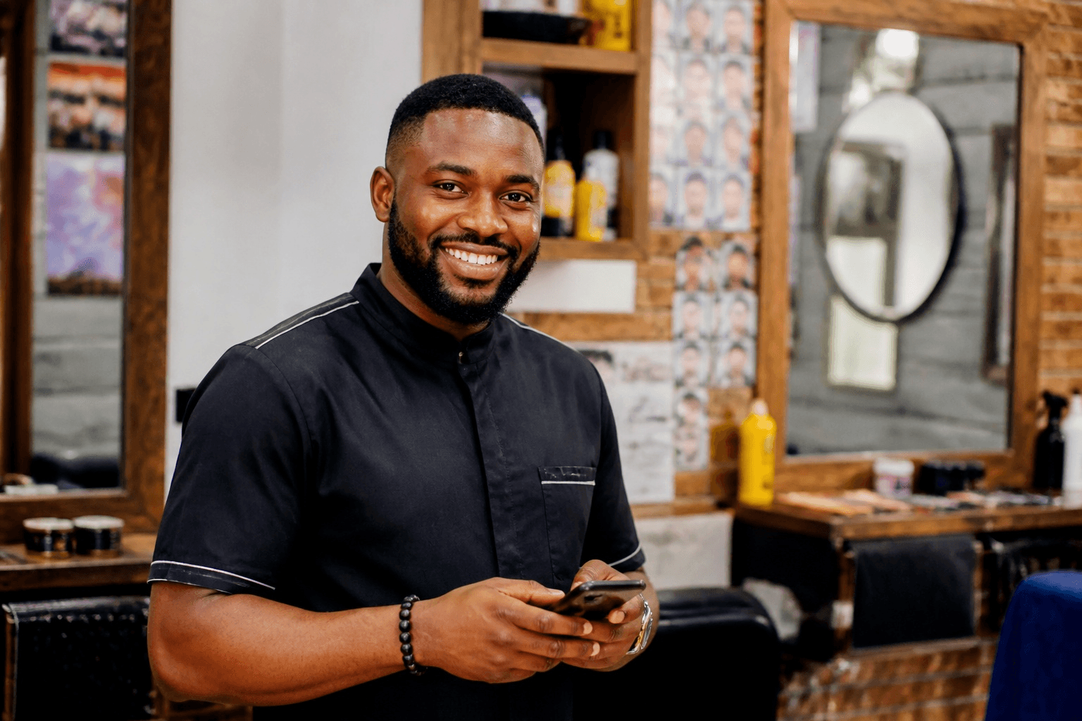 Portrait de Franck Soro, coiffeur, souriant avec son téléphone à la main